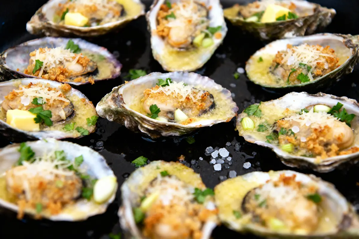 Huîtres gratinées au four avec persil, fromage râpé et beurre, disposées sur un plateau noir.