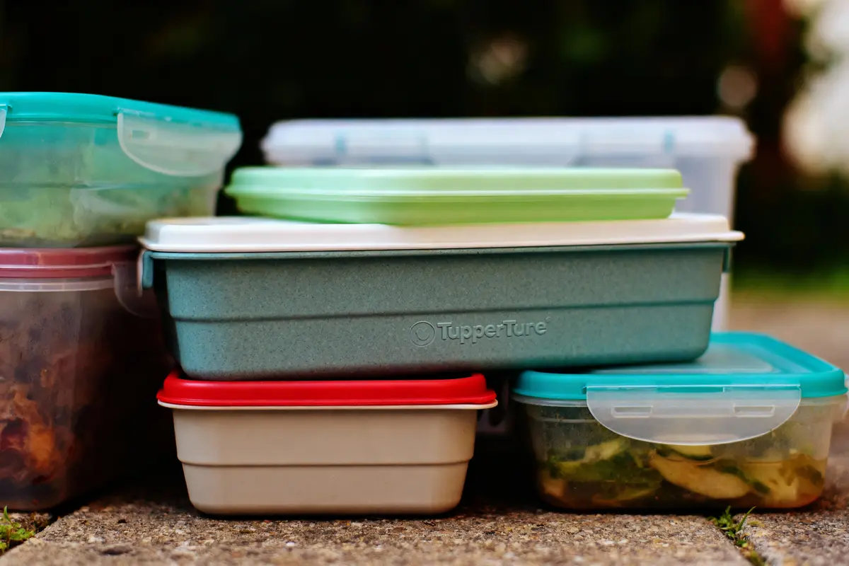Plusieurs boîtes alimentaires colorées empilées sur un sol en extérieur, contenant divers aliments.