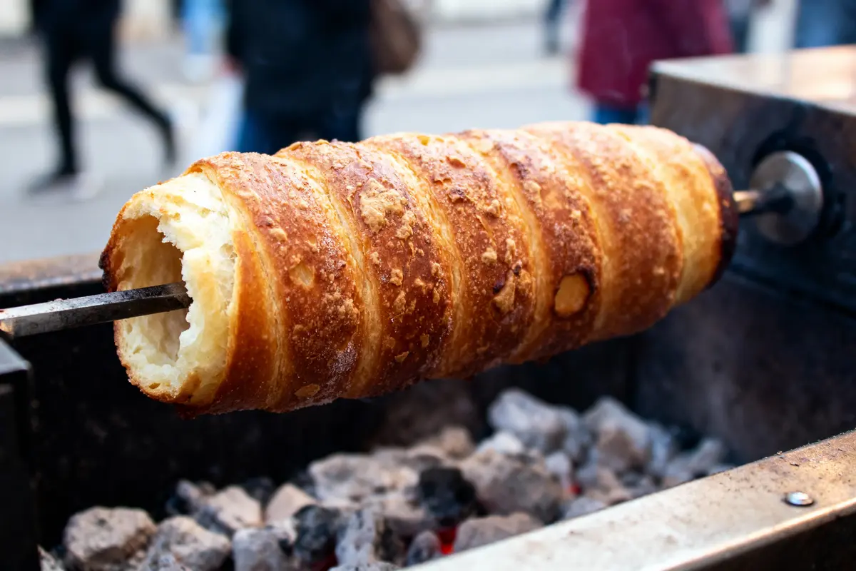 Brioche dorée rotative cuite au feu de bois, sur broche, marché de rue en arrière-plan flou.