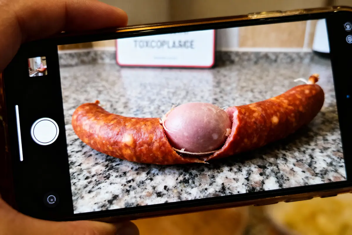 Photo sur téléphone d'une saucisse ouverte contenant un œuf, posée sur un comptoir de cuisine.