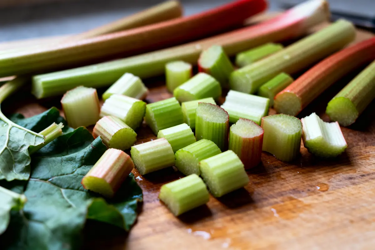 Tiges de rhubarbe coupées en morceaux et feuilles vertes sur une planche en bois.