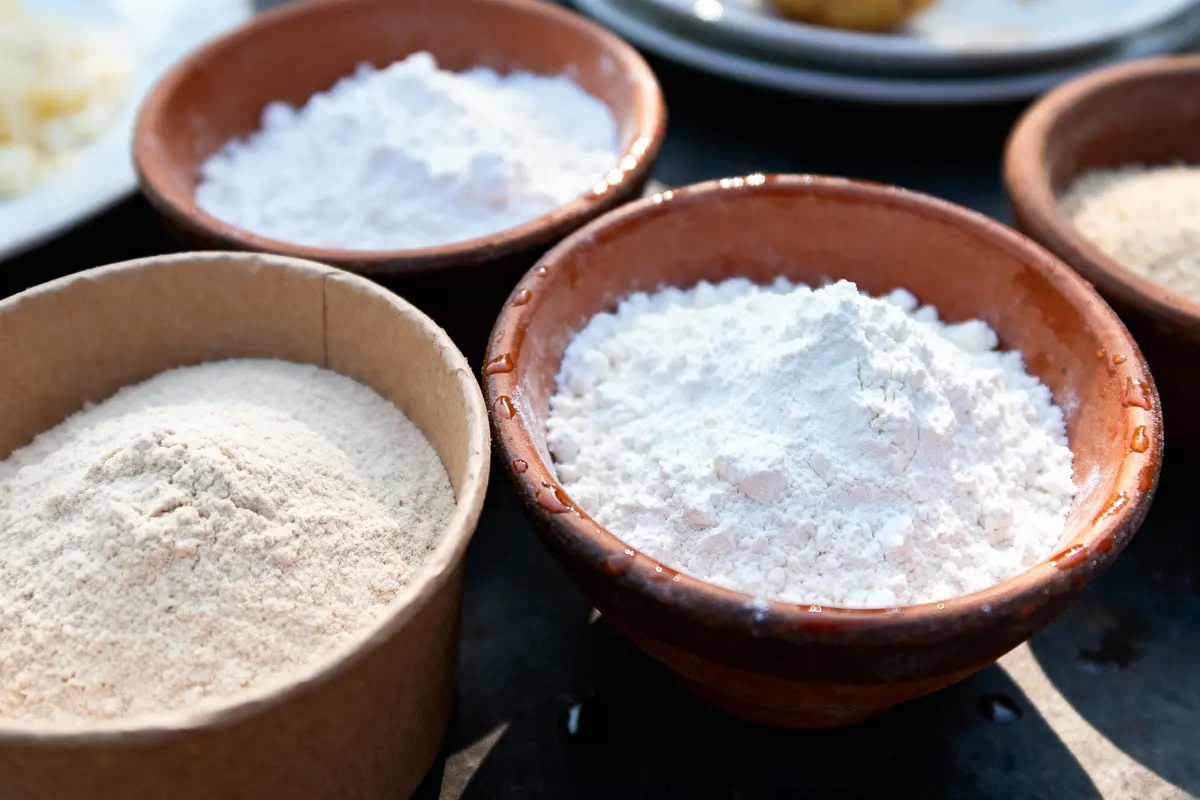 Trois bols en terre cuite contenant des différentes variétés de farine, posés sur une table.