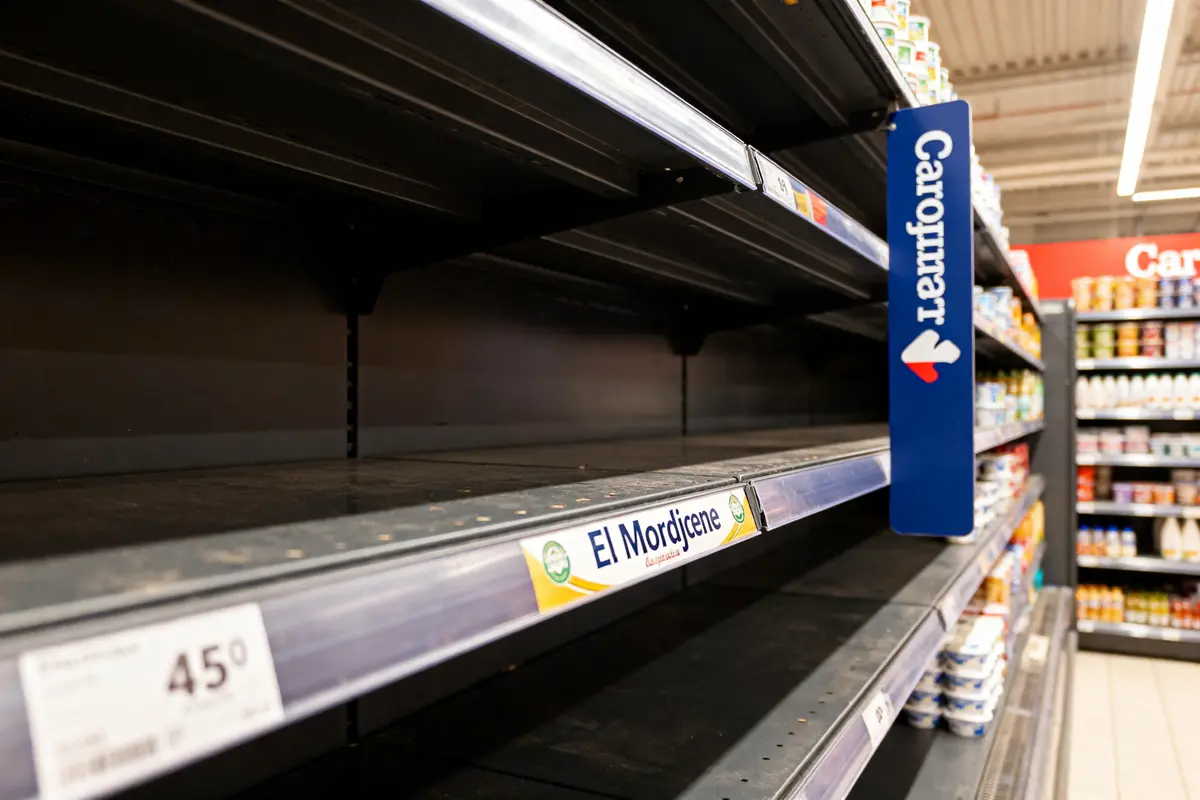 Étagères de supermarché vides avec quelques produits restants et étiquette "Carrefour".