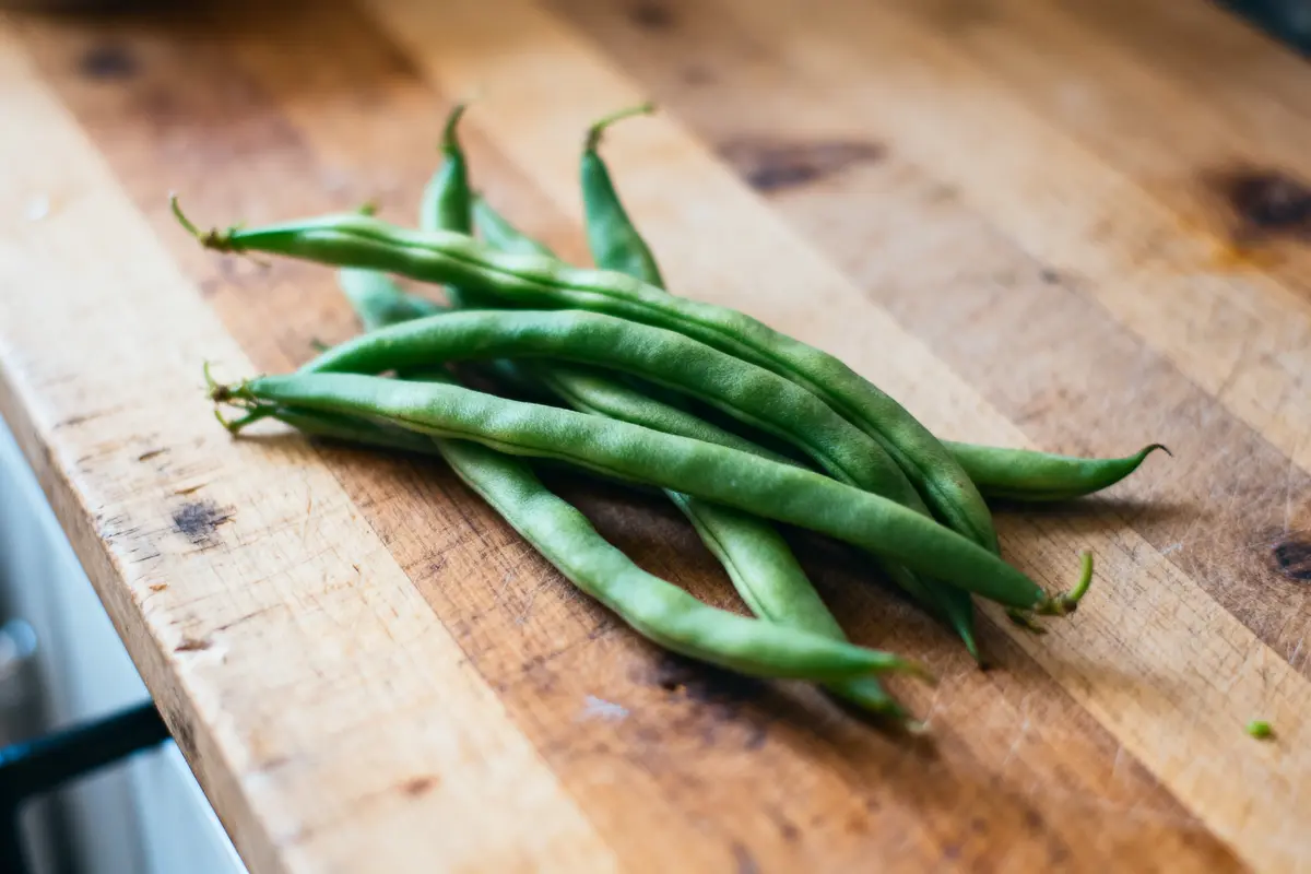 Haricots verts frais sur une planche à découper en bois, lumière naturelle douce.