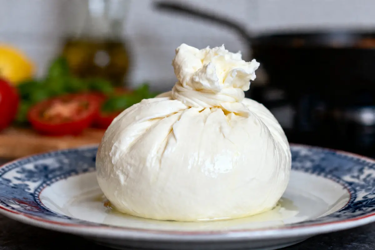 Une burrata crémeuse sur une assiette décorative avec des tomates en arrière-plan flou.