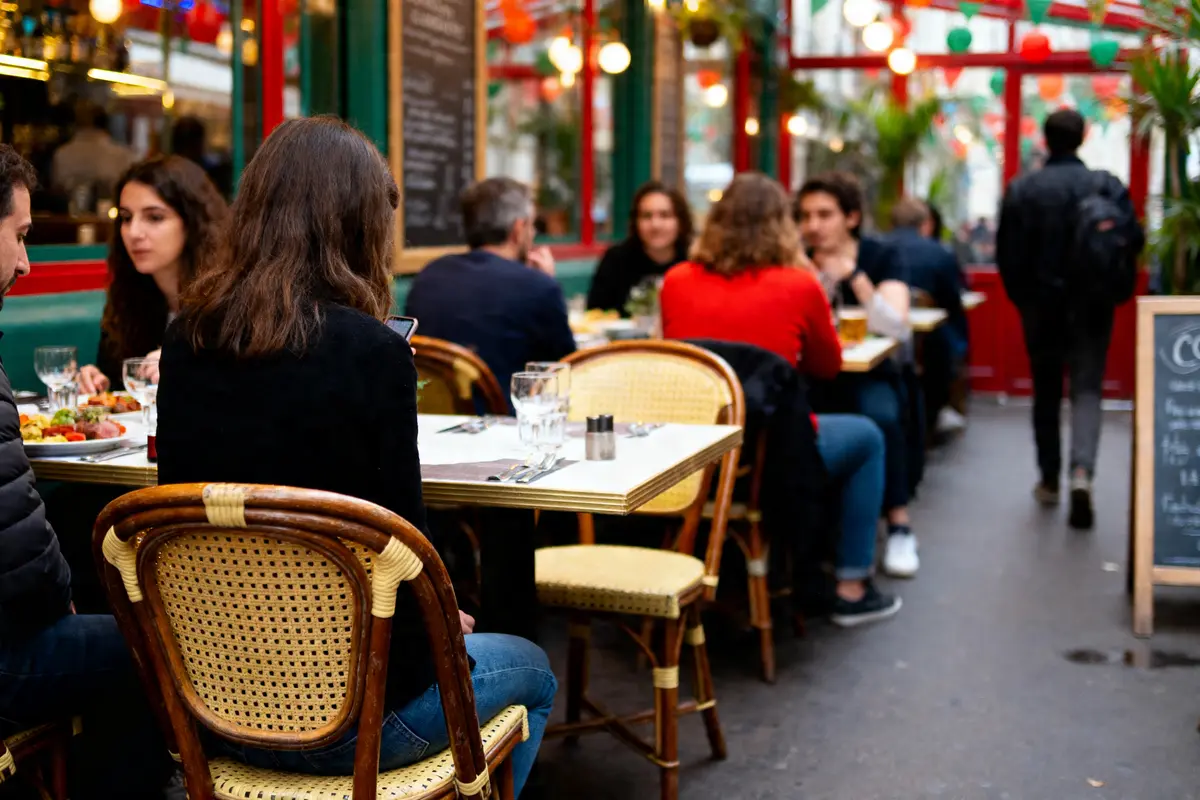 Des personnes dînent à une terrasse de restaurant animée, entourées de décorations colorées.