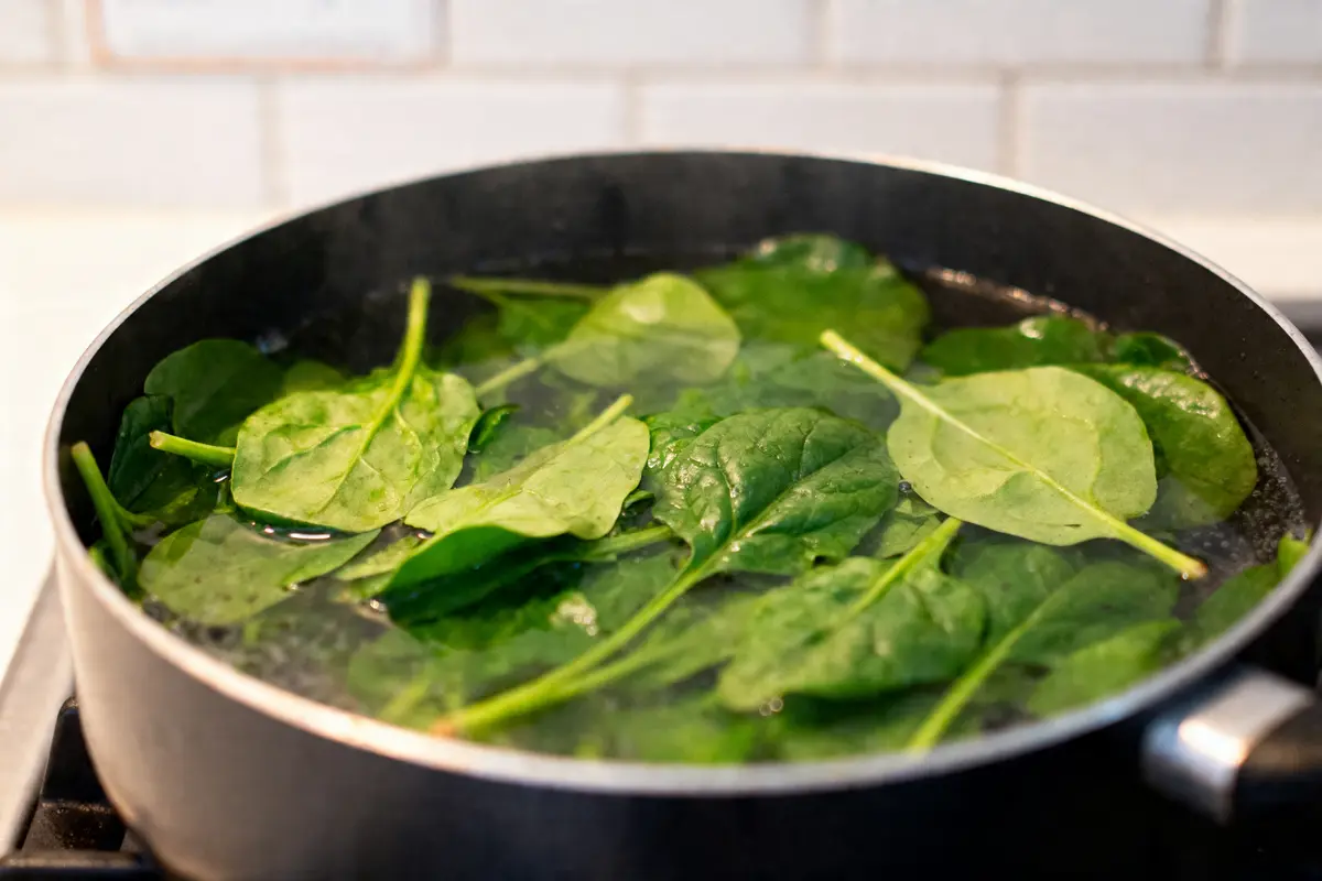 Épinards frais cuisant dans une casserole d'eau bouillante sur la cuisinière.