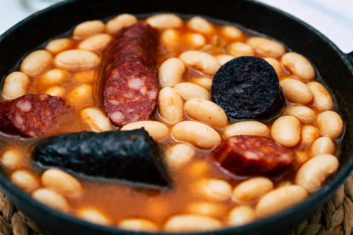 Plat de haricots blancs mijotés avec morceaux de saucisse et chorizo, dans une sauce tomate épicée.
