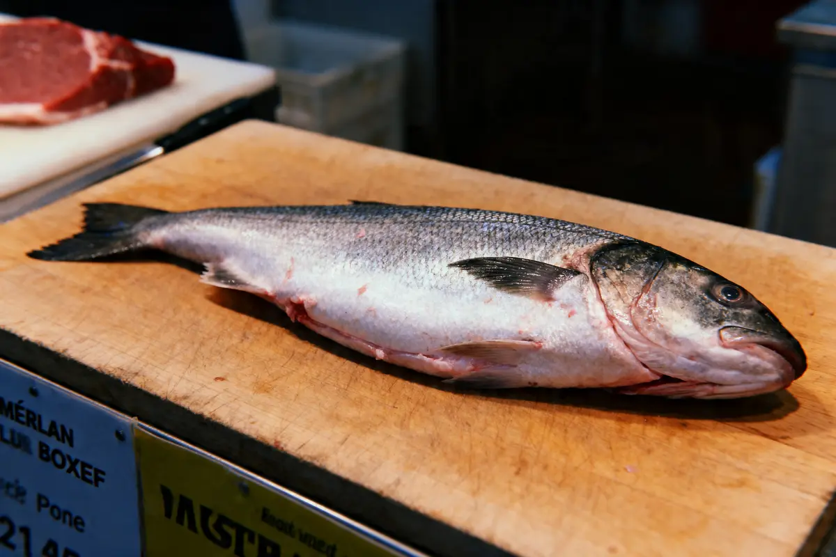 Poisson entier sur une planche à découper en bois, près d'un morceau de viande crue.
