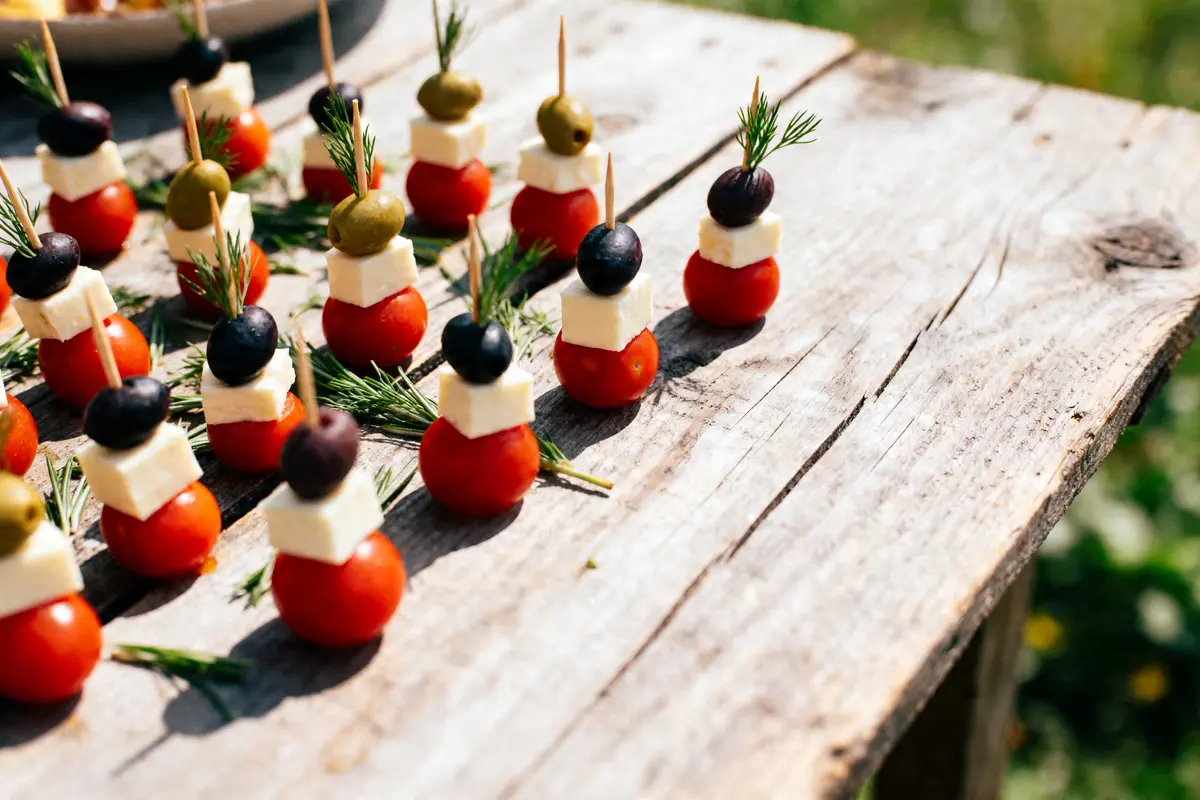 Bouchées de tomates cerises, fromage, olives noires et vertes, sur pique, décorées avec herbes sur table en bois.