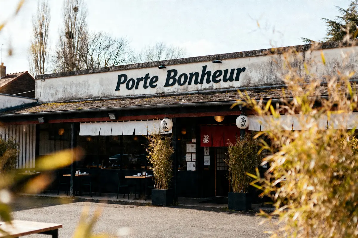 Façade du restaurant "Porte Bonheur" avec bambous devant, ambiance asiatique et nom visible sur l'enseigne.
