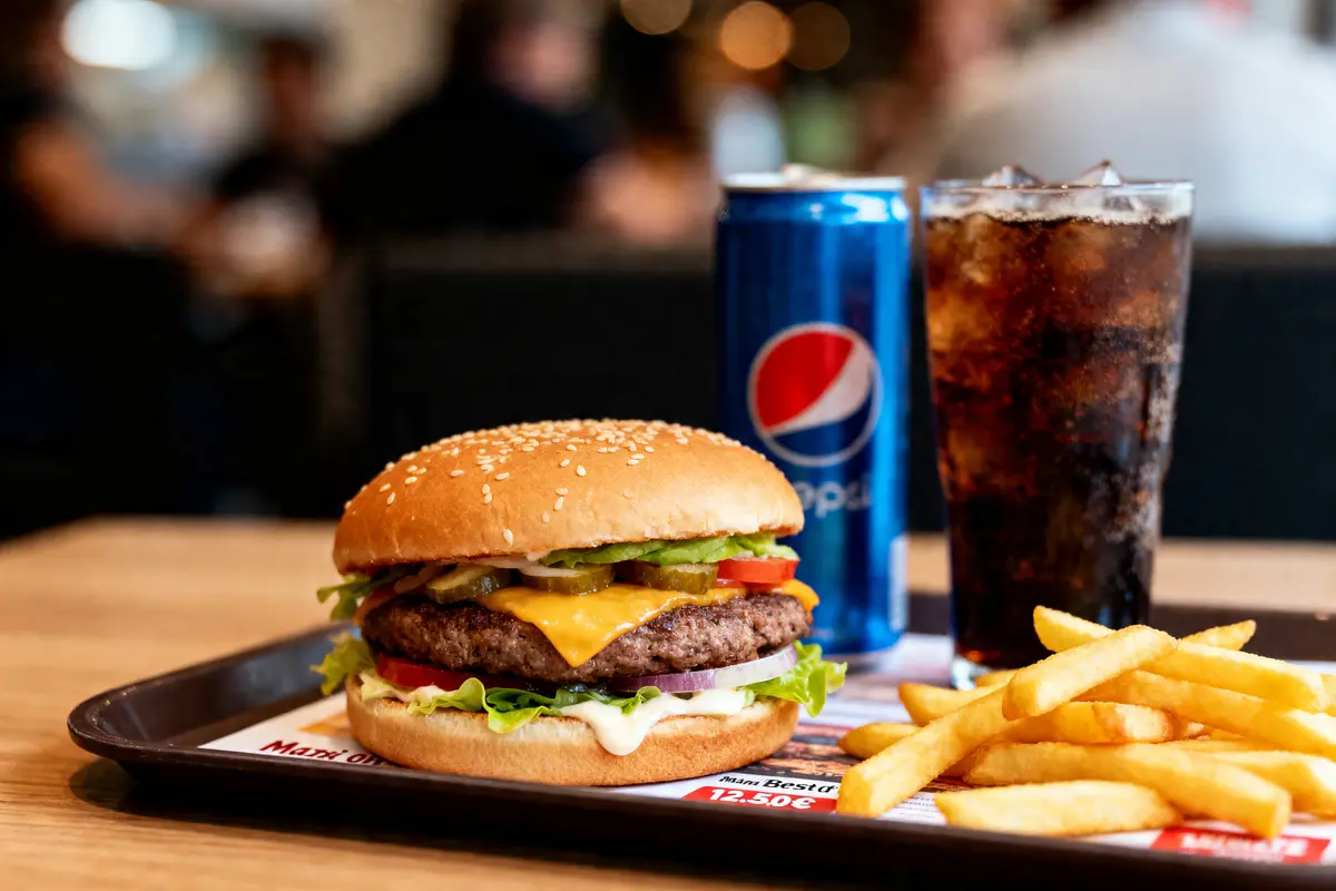 Burger avec fromage, frites, boisson gazeuse Pepsi sur un plateau dans un restaurant, ambiance floue en arrière-plan.