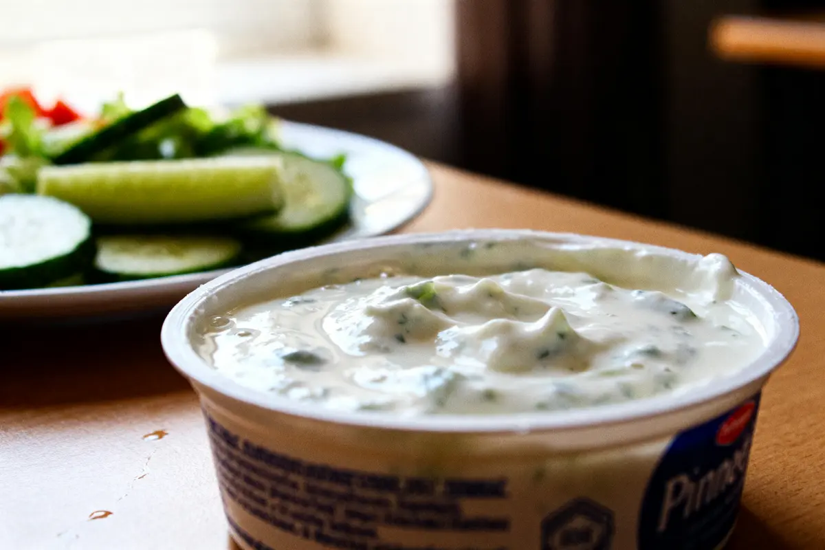 Bol de raitia crémeux à côté de tranches de concombre et salade verte