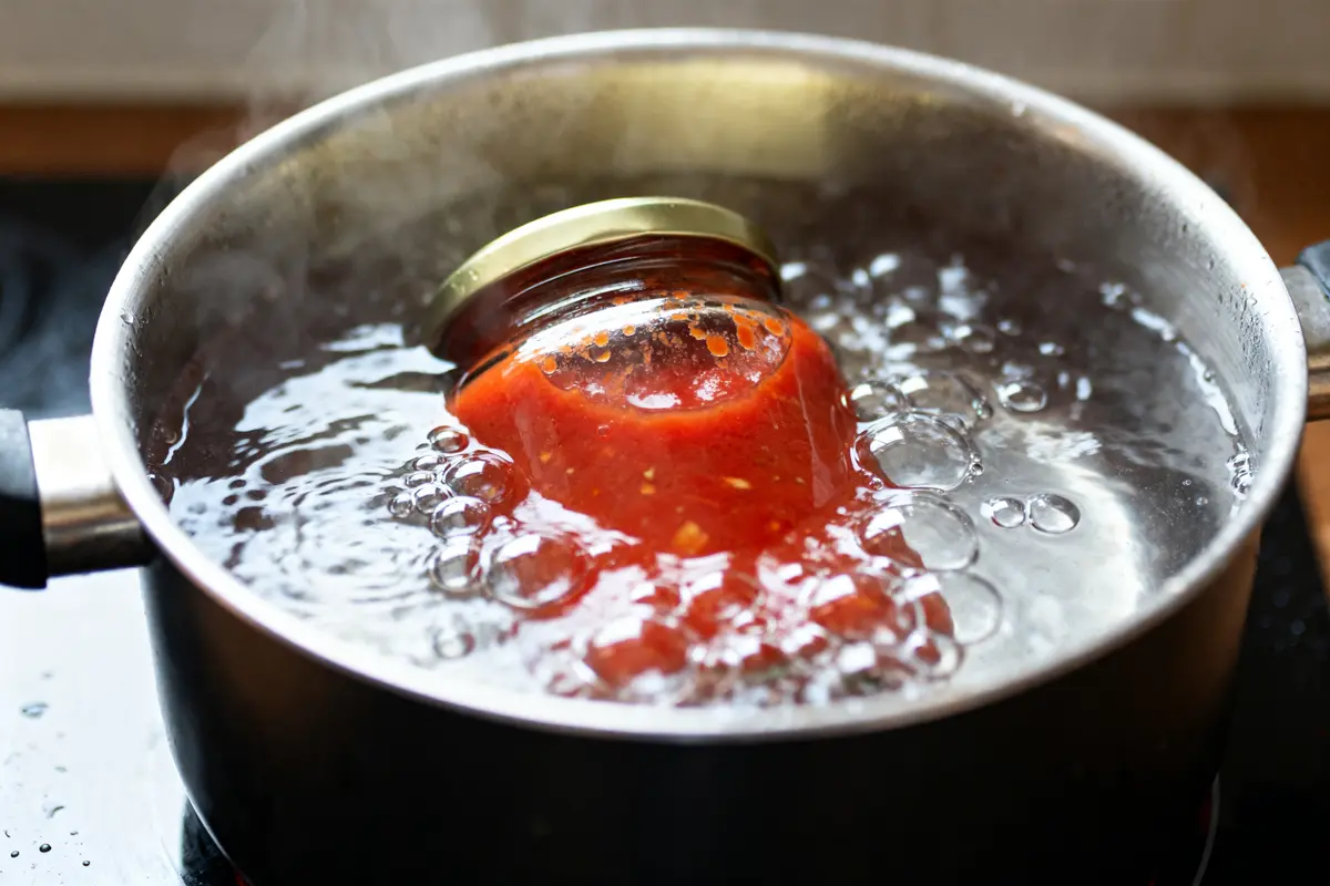 Bocal stérilisant de sauce tomate dans une casserole d'eau bouillante pour le temps requis